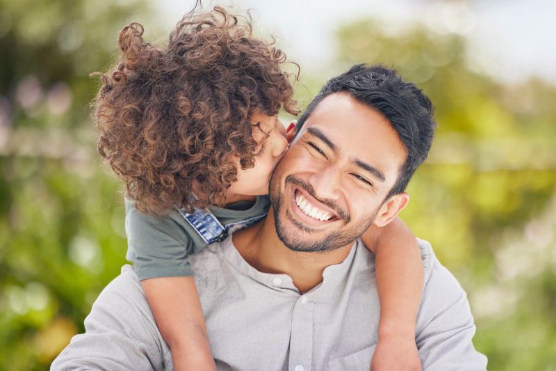 Young child kissing a smiling father on the cheek outdoors