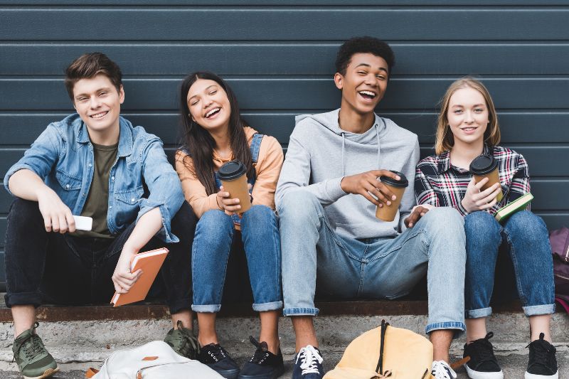 Four smiling teenagers sitting outdoors holding coffee cups and books Advanced Orthodontics in Kent, WA