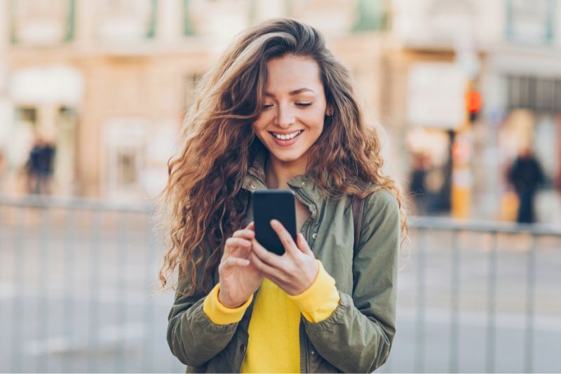 Young woman smiling while using her smartphone outdoors Advanced Orthodontics in Kent, WA