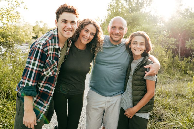 Family of four smiling together outdoors on a sunny nature trail, Advanced Orthodontics in Kent, WA
